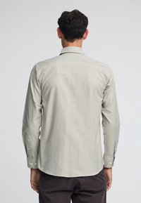 Camicia a maniche lunghe di un colore crema chiaro con un motivo a piccoli quadrati, in tessuto morbido, colletto con bottoni e polsini abbottonati.