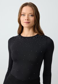 Maglietta nera a maniche lunghe con una texture liscia, caratterizzata da strass sparsi intorno al collo per un tocco decorativo.