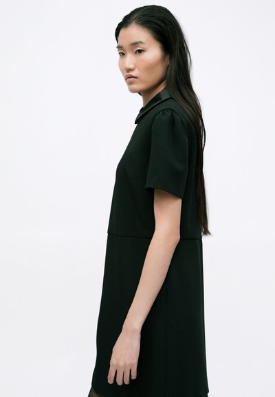 Rochie neagră cu mâneci scurte tip puff, guler la gât și corp ajustat. Material neted, lungime până la mijlocul coapsei, cusături minime.