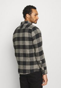 Wool-blend shirt in black and grey check pattern. Features a collared neck and buttoned cuffs. Textured fabric with a straight hem.