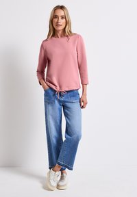 Ljusrosa sweatshirt med rund halsringning och trekvartsärmar, i kombination med vida blå denimjeans och vita sneakers.