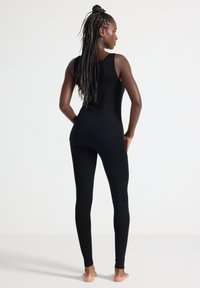 Svart topp och leggings-set, med en åtsittande design och slät textur. Outfiten har inga synliga mönster eller hårdvarudetaljer.