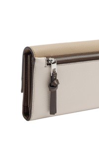 Beżowo-kremowy portfel z ekoskóry o teksturowanej powierzchni, z srebrnym zamkiem błyskawicznym i brązowym paskiem akcentującym. Posiada wiele kieszonek na karty wewnątrz.