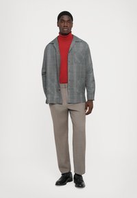 Gray plaid coat over a red turtleneck, paired with light beige trousers and black shoes, showcasing layered, structured design and textured fabric.
