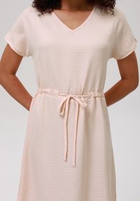 Light pink dress made of textured fabric, featuring a V-neck, short sleeves, and a tied waist drawstring for adjustable fit.