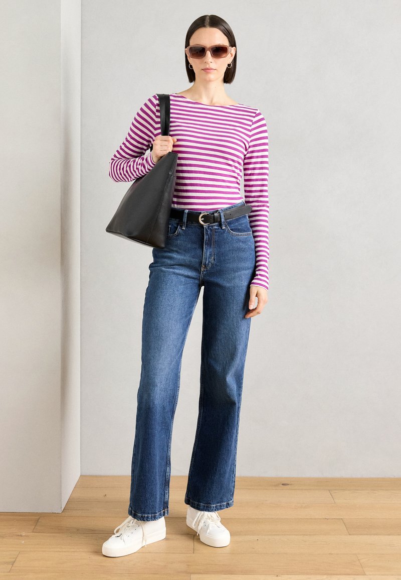 Gestreiftes Langarmshirt in Lila und Weiß, hochgeschnittene blaue Jeans, schwarze Handtasche und weiße Sneakers mit Schnürsenkeln.