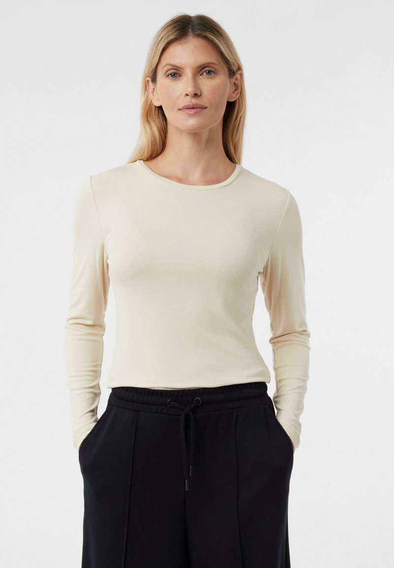 Jasnobeżowa bluzka z długim rękawem o okrągłym dekolcie i dopasowanym kroju. Miękka, teksturowana tkanina zestawiona z czarnymi spodniami ze ściągaczem.