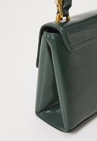 Grön patentläderhandväska med en strukturerad form, med en vikflik och detaljer i guld. Texturerad yta ger extra detalj.