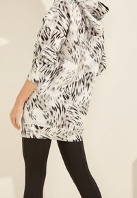 Witte hoodie met lange mouwen in een zwart-wit abstract patroon, voorzien van een capuchon met trekkoord en elastische manchetten, gecombineerd met zwarte leggings.