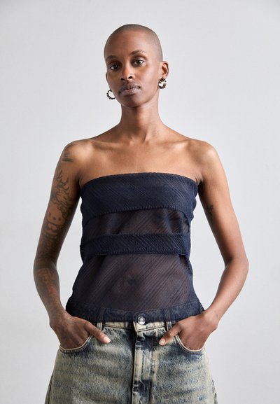 Top blu navy senza spalline con tessuto testurizzato, pannelli sovrapposti e sezioni trasparenti, abbinato a jeans in denim chiaro con una finitura distressed.