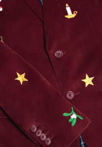 Burgundowy blezer z korduroju z haftowanymi wzorami świecy, żółtej gwiazdy i jemioły, z brązowymi guzikami i teksturowanym materiałem.