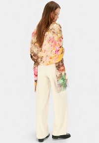 Szal z kwiatowym wzorem wykonany z miękkiego materiału, z żywymi kolorami takimi jak różowy, żółty i zielony. Długie frędzle zdobią krawędzie.