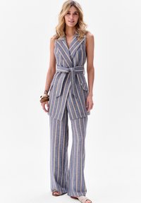 Gestreepte blauwe vest en set met wijde broek met een ceintuur in de taille, met gele strepen en dubbele voorzakken. Gladde, lichte stof.