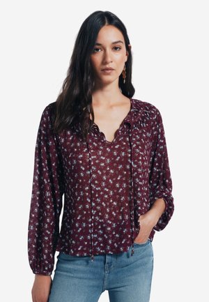 Bordeaux bloemenblouse met lange mouwen, gerimpelde halslijn en trekkoorddetails. Heeft kleine blauwe bloemen en een ontspannen pasvorm.
