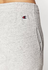 Grå atletiske joggebukser laget av myk, teksturert stoff. Funksjoner inkluderer elastisk midjebånd, sidelommer og en liten brodert logo.