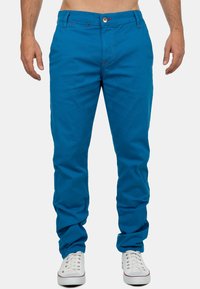 Heldere blauwe katoenen chino broeken met rode stikdetails en een knoopsluiting. Soepele textuur en taps toelopende pasvorm. G gedragen met witte sneakers.
