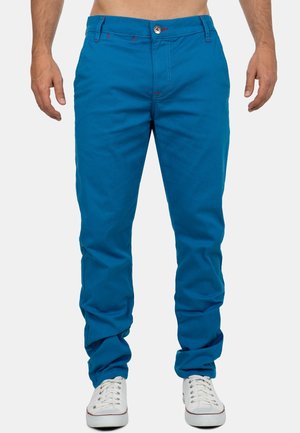 Heldere blauwe katoenen chino broeken met rode stikdetails en een knoopsluiting. Soepele textuur en taps toelopende pasvorm. G gedragen met witte sneakers.
