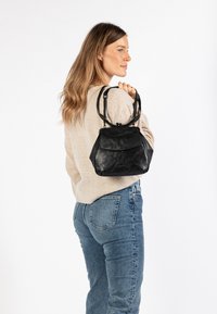 Borsa a mano in pelle nera dalla forma arrotondata, con chiusura a cerniera superiore e manici corti doppi. Superficie testurizzata con dettaglio della tasca frontale con pattina.