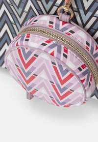 Porte-monnaie zip rond avec un motif géométrique multicolore dans des tons de rose, rouge et gris. Dispose d'une fermeture éclair dorée et de matériaux lisses et texturés.