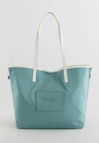 Stor tote taske i lyseblå nylon med hvide læderhåndtag, et rektangulært mærke på forsiden prægede med "FRIENDLY PROJECT STYLE: BAG."
