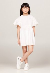 Balta medvilninė suknelė su raukiniais rankovėse, akelėmis hemelyje ir minkštu audiniu. Derinama su baltais sportbačiais kasdienei išvaizdai.