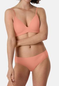 Pfirsichfarbener BH mit glatter Textur und V-Ausschnitt-Design, kombiniert mit passender nahtloser Bikinitranshorts. Verfügt über dünne Träger und minimalistische Details.