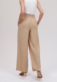 Beżowe spodnie o szerokich nogawkach z teksturowanej tkaniny, z elastycznym paskiem w talii i bocznymi kieszeniami. Zestawione z cielistymi sandałami na wysokim obcasie.