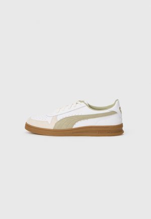 White and beige sneaker with green accents, suede and leather materials, round toe, rubber sole, and perforated details on the upper.