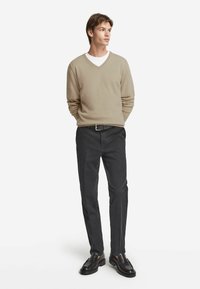 Beige v-ringad tröja, svarta byxor och mörka skor. Tröjan har ett mjukt, texturerat tyg; byxorna är skräddarsydda med rak passform.