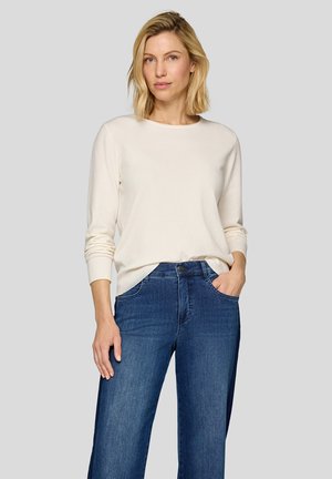 Light beige sweater with long sleeves, ribbed cuffs, and a relaxed fit, paired with dark blue wide-leg jeans, front pockets visible.
