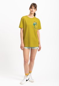 Geel katoenen T-shirt met een ontspannen pasvorm, voorzien van een grafische print in blauw, groen en rood. Gecombineerd met lichte shorts en hoge sneakers.