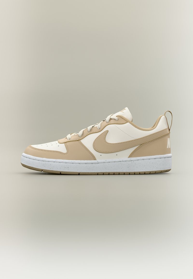 Nike Sneaker in Weiß und Beige, niedrig geschnitten, mit Schnürsenkeln, Swoosh-Logo und weiß gesprenkelter Sohle auf neutralem Hintergrund.