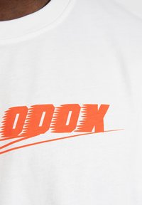 Hvid bomulds T-shirt med et stort orange grafik, der står "ODDOX" i en fed, vinklet skrift. Har en rund halsudskæring og en glat tekstur.