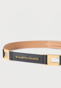 Μαύρη δερμάτινη ζώνη με χρυσαφένια μεταλλική αγκράφα, με λογότυπο σε ανάγλυφο σε μια λείο, καφετί λουρί που αντιπαραβάλλεται. Κομψός και ορθογώνιος σχεδιασμός.