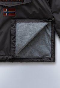 Zwarte buitenjas van stof met een zachte grijze fleece voering. Voorzien van een Noorse vlag patch en een ritszak. Over het geheel genomen een soepele textuur.