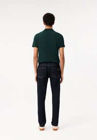 Polo verde de manga corta combinado con jeans de mezclilla azul oscuro. La camisa tiene un cuello clásico y los jeans cuentan con dos bolsillos traseros.