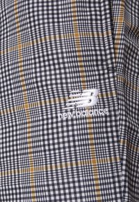 Black and white checkered fabric with yellow accent lines. Features embroidered white "New Balance" logo on the side.