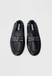 Czarne wsuwane buty ze skóry o gładkiej fakturze, z paskiem ozdobionym ćwiekami i wytłoczonym logo. Okrągły nosek i wyściełany kołnierz.