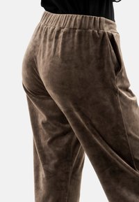 Pantalones de terciopelo marrón con cintura elástica, bolsillos laterales y textura suave, mostrados de perfil.