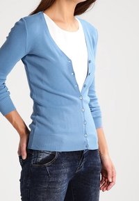 Ljusblå cardigan i mjukt stickat material, med V-ringning, full knappfront och ribbade ärmslut och fåll. Matchad med mörka jeans.