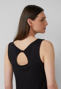 Haut sans manches noir avec un col rond et une découpe en trou de serrure à l'arrière, présentant un détail en nœud au-dessus de l'ouverture. Texture lisse.