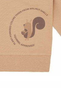 Beige sweatshirt met een afbeelding van een bruine eekhoorn die een walnoot vasthoudt. Tekst leest: "Plantenkracht kleuren gehaald uit walnootschalen! Eekhoorn-goedgekeurd!"