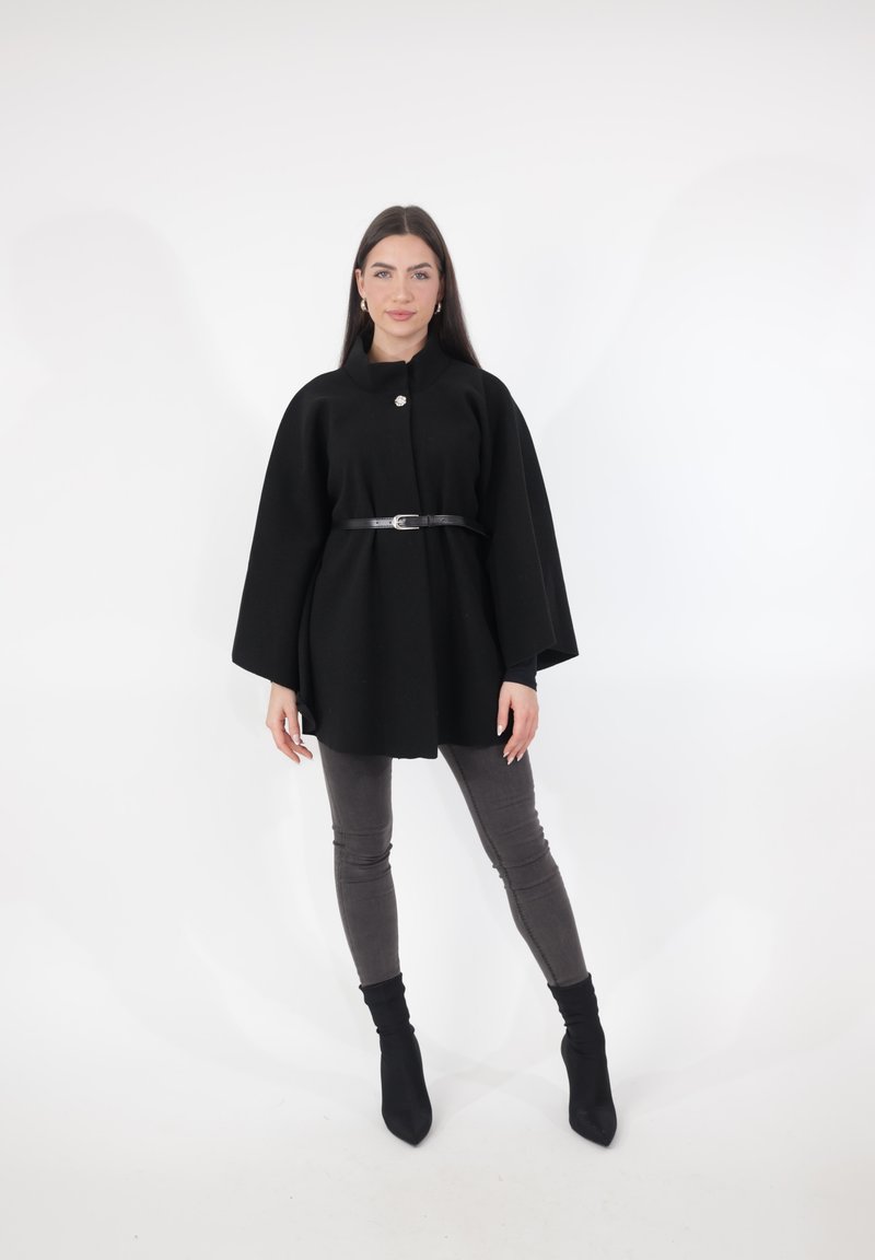 Sort uld kappe med rund krave, enkelt knaplukning og sort læderbælte. Kombineret med grå skinny jeans og sorte ankelstøvler.