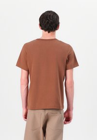 Bruine T-shirt met korte mouwen en een klassieke ronde hals, gladde textuur en een relaxte pasvorm, van achteren getoond tegen een witte achtergrond.