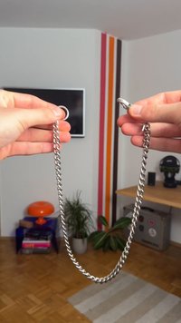 Řetěz z jemného stříbrného kovu s hladkým, lesklým povrchem; má kulatou kroužek a sponu na dráp. Řetěz má propletené články a masivní design.