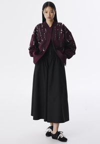 Cazadora bomber burdeos con lentejuelas, vestido negro fruncido y zapatillas negras con cordones blancos. Diseño simple y minimalista.