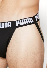 Schwarzer Puma-Tanga mit einem weichen elastischen Bund und weißem Logo, schlankem Design und minimaler Abdeckung, der die Stoffstruktur und Passform hervorhebt.