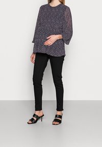 Blusa a stampa floreale con maniche lunghe trasparenti, scollatura rotonda e vestibilità ampia, abbinata a pantaloni neri attillati e décolleté neri con fasce.