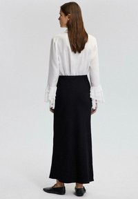 Blusa blanca con mangas acampanadas combinada con una falda larga negra. La blusa es ligera, mientras que la falda tiene una textura suave.