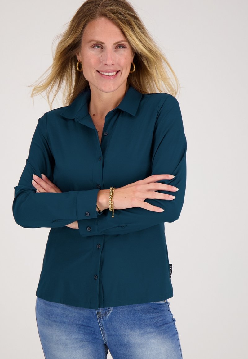 Teal knoopshirt met een kraag, lange mouwen en zwarte knopen. Gestyled met relaxte blauwe jeans. Soepele textuur, geen zichtbare patronen.